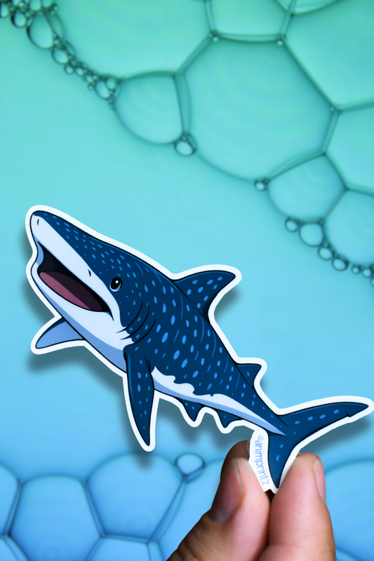 A die-cut sticker of a cartoon whale shark being held by a person's fingers against a blue background with bubble graphics.